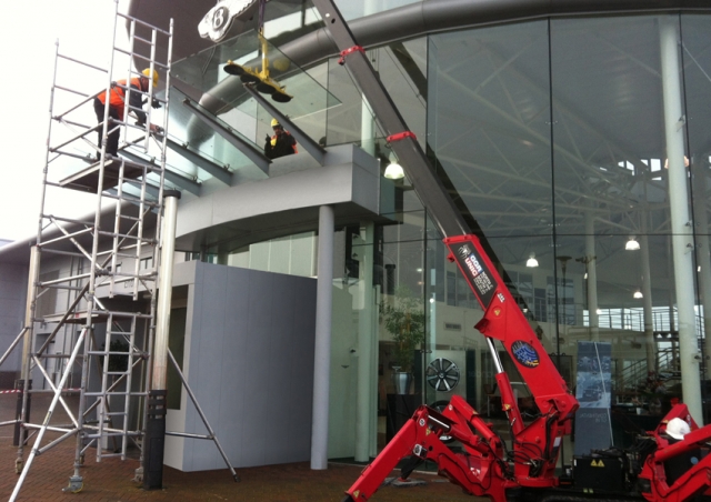 A URW-095 mini spider crane installing canopy glass at a Bentley dealership