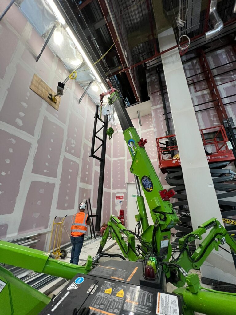 The UNIC Tracked ECO-295 Mini Spider Crane lifting steel beams inside a first-floor store in Westfield London shopping centre.