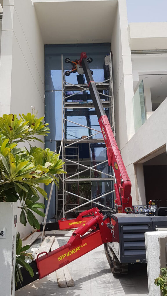 A URW-546 Mini Spider Crane installing glass with the GL-UMC 600 Glass Manipulator in Dubai by UNIC Cranes Europe's dealer Spider Plus.